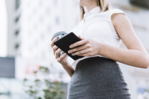 Home - low angle view businesswoman holding smartphone disposable coffee cup outdoors scaled