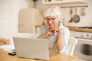 Home - modern technology old people retirement gray haired female pensioner glasses filling loan application form online sitting front laptop reading information with serious focused look scaled