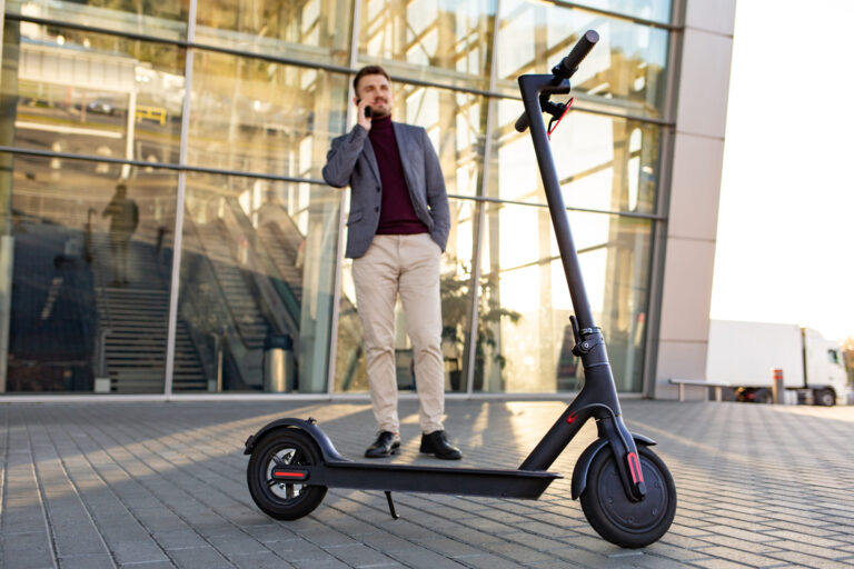 News - young handsome man with e scooter standing sidewalk near airport sunset talking smartphone 1 scaled